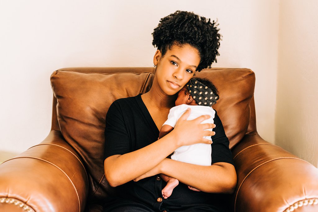 black mom holding newborn in brown leather chair