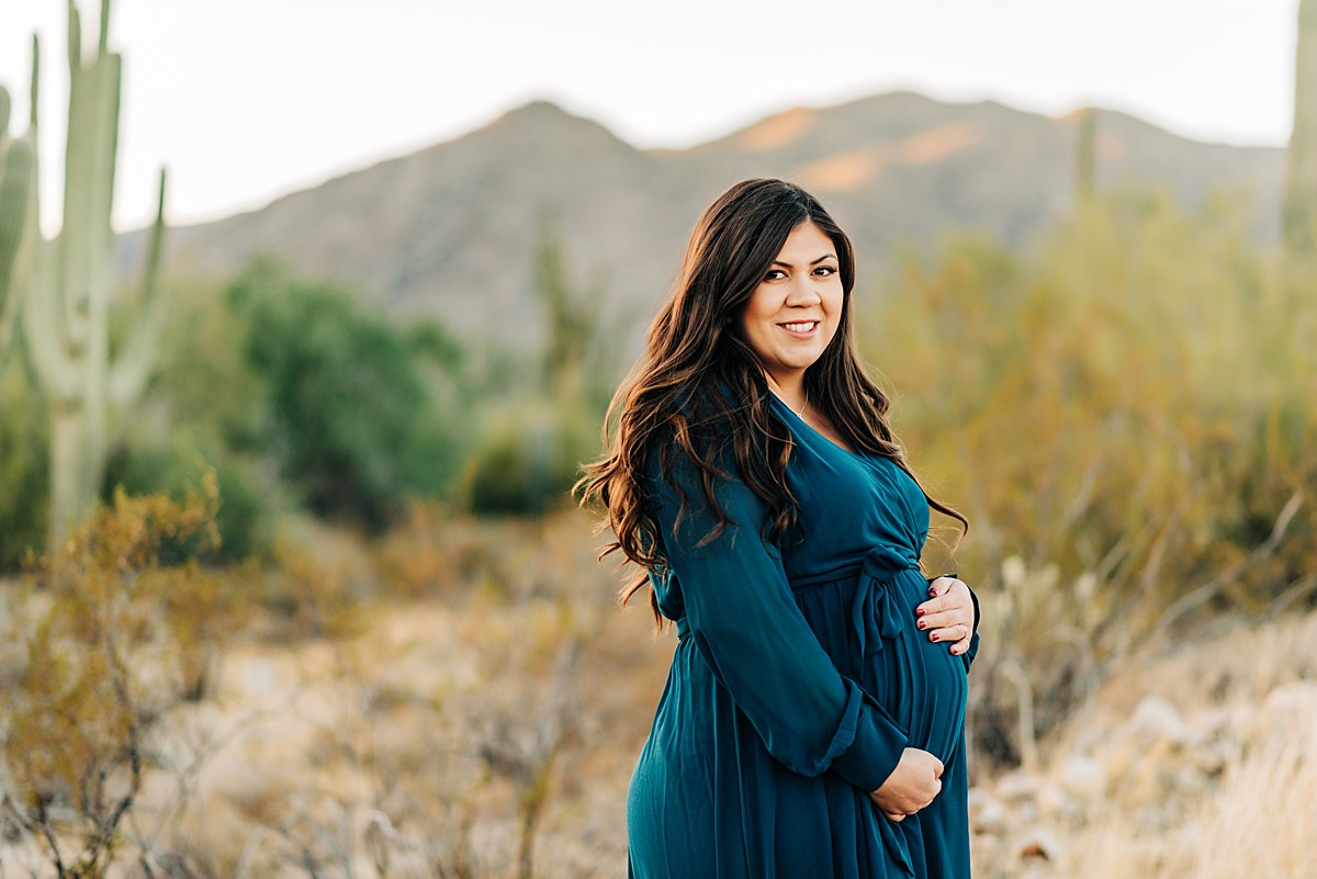 pregnant mom wearing a teal dress and holding baby bump in an arizona desert maternity session at white tank mountains