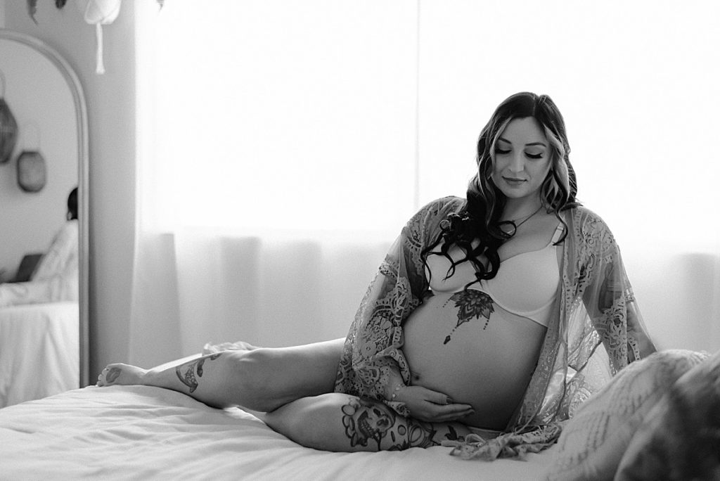 black and white mom sitting on bed and hugging baby bump