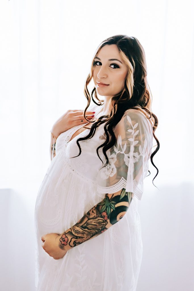 pregnant woman in white lace dress by window