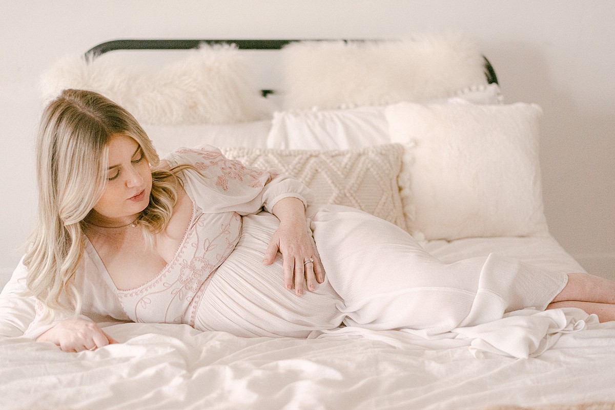 expecting mom in light flowy gown on bed while holding and gazing at baby bump