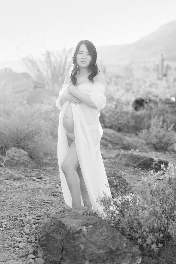 White chiffon fabric draped over pregnant woman with baby bump exposed. She is standing in Phoenix, AZ desert