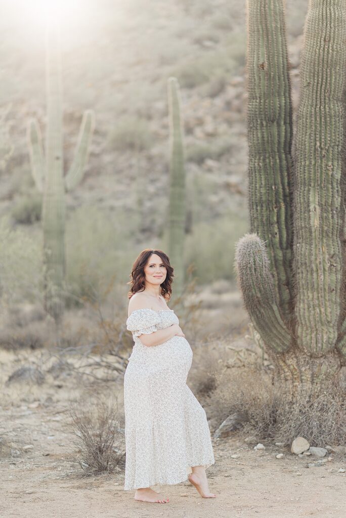 expecting mom standing next to large saguaro cactus for desert maternity photos