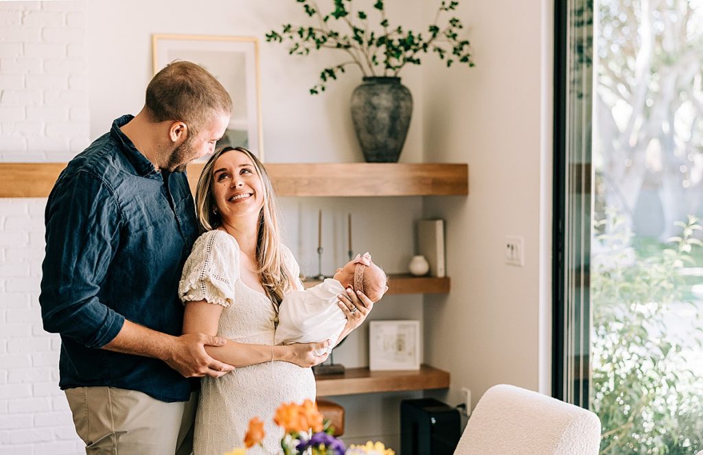 New parents cuddled together holding newborn baby in home with neutral decor.