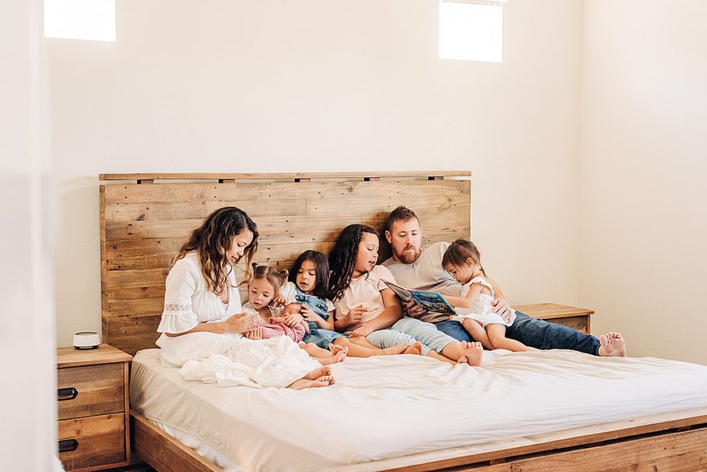family of 7 lounging on bed with neutral decor for in home newborn photos