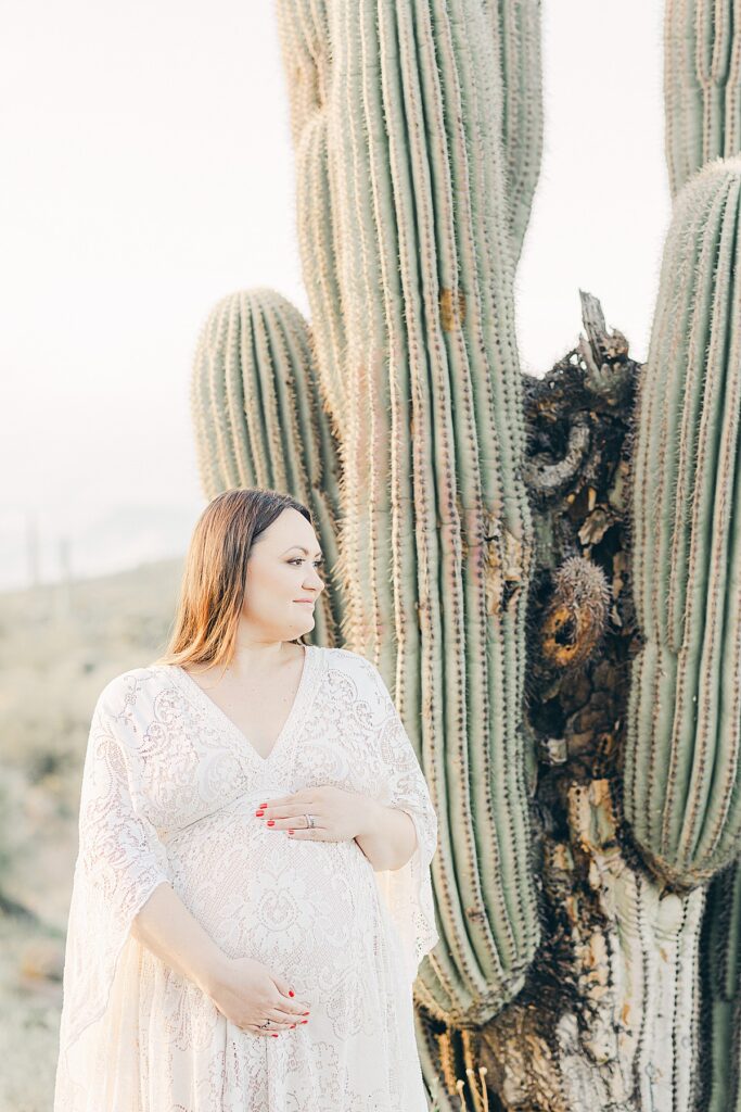 closeup of expecting mom in boho cream lace dress next to saguaro cactus as a favorite desert maternity photoshoot location