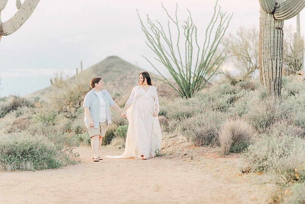 expecting couple walking through spring day at brown's ranch trailhead a perfect location for desert maternity photoshoot. theyre surrounded by lush desert terrain