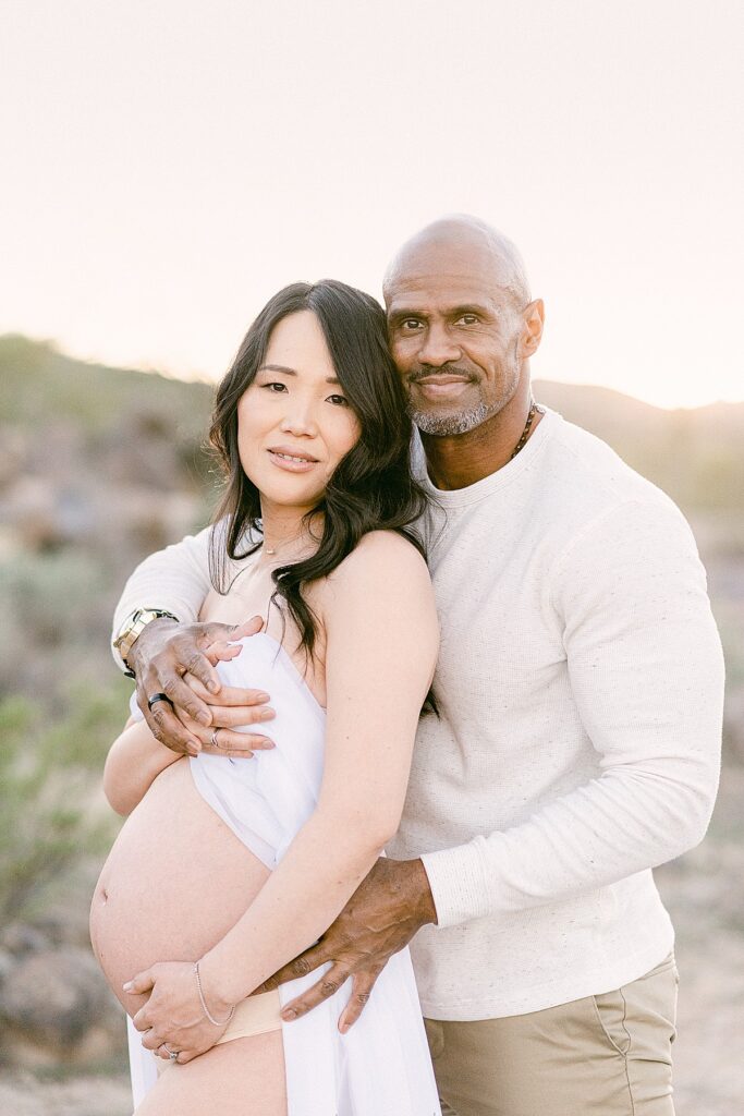 couple embraced and holding exposed baby bump for maternity boudoir in the desert