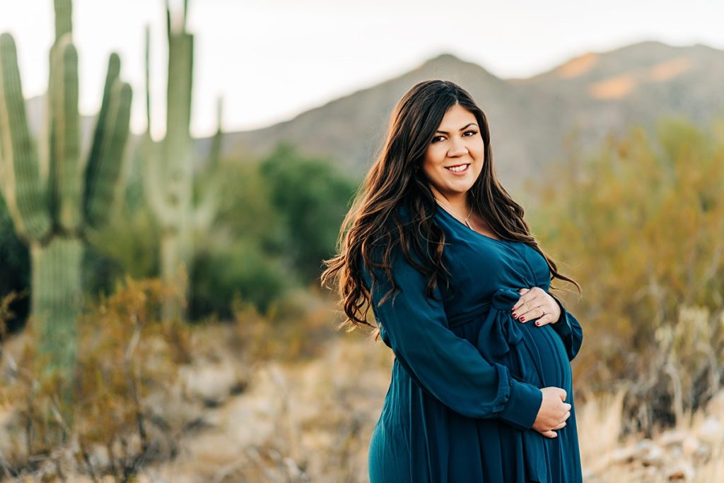 expecting mom cradling baby bump with desert scenery in background