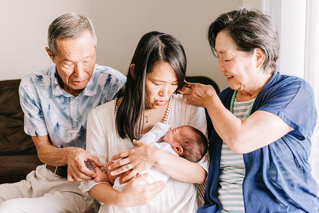 Grandparents tending to mother who is holding newborn baby. Grandmother is pushing back mother's hair. Mother is shushing newborn baby. Grandfather is playing with newborn baby toes.