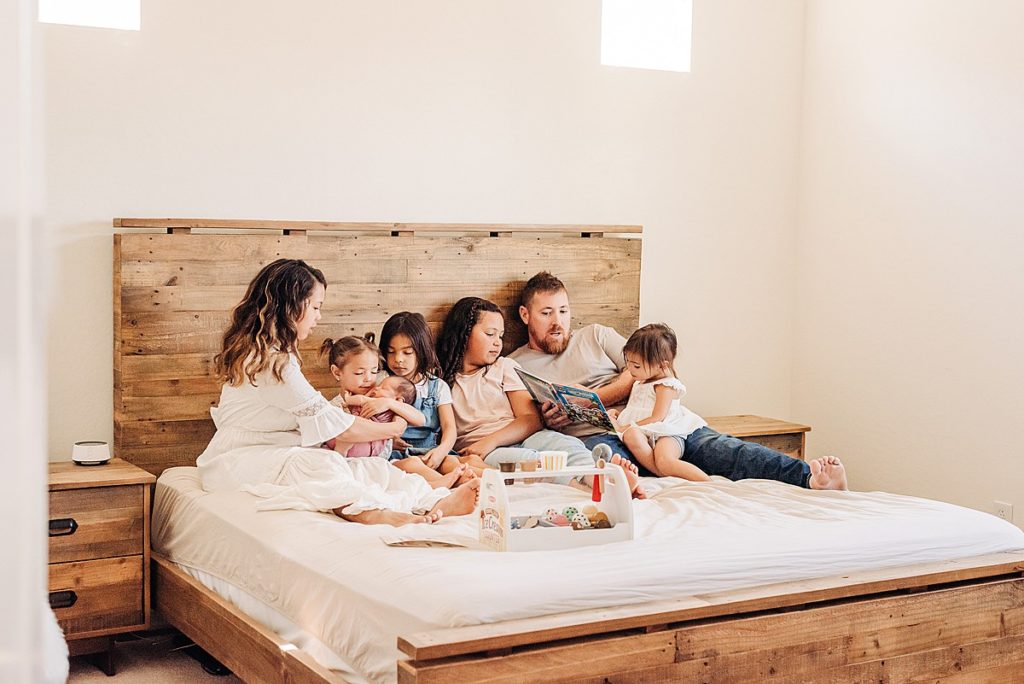 Candid moment of family of 7 lounging on bed for lifestyle newborn photos in home.