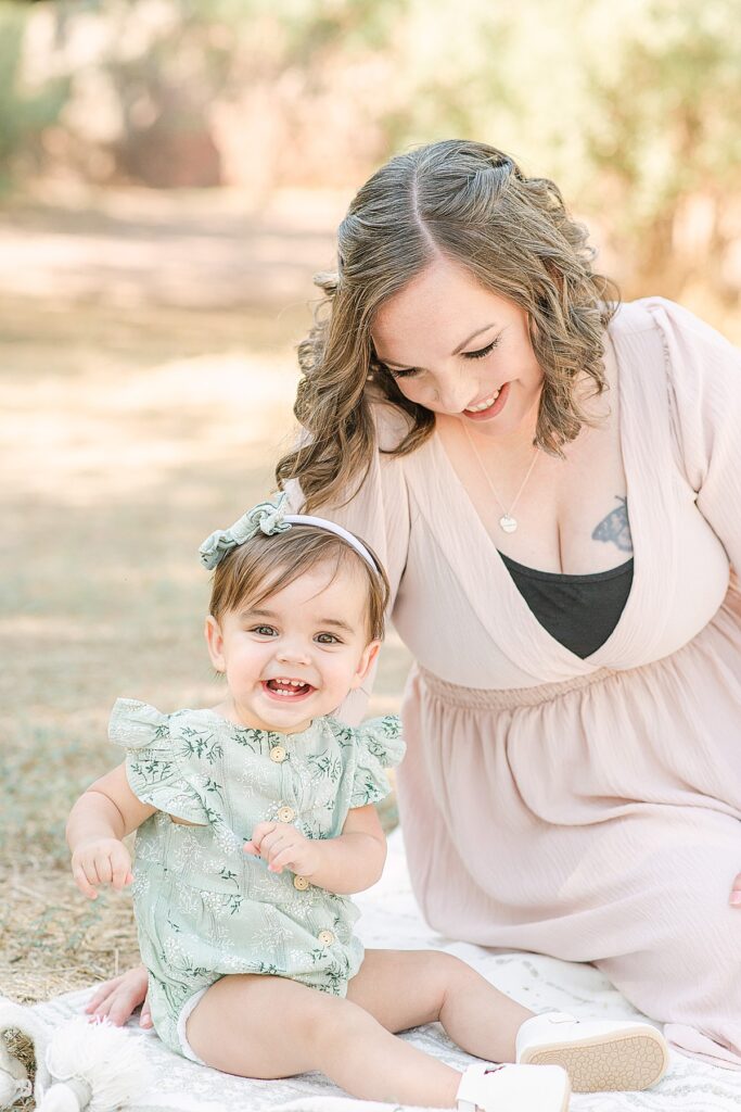 Toddler dancing while sitting next to mom who's smiling looking down at her.