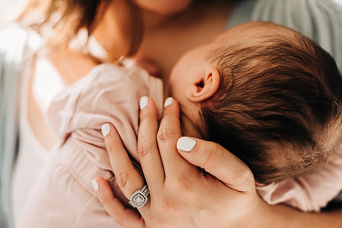 closeup of mom's hands around baby's upperback holding newborn baby girl.