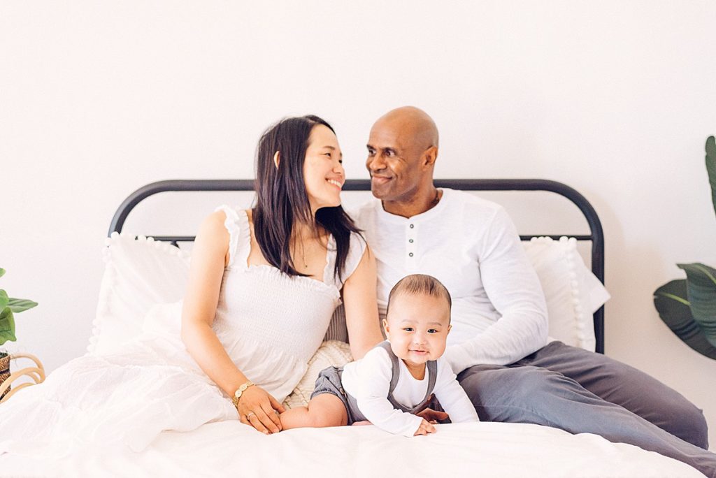 Candid couple with 6 month baby boy snuggling on bed. Baby is lifted up on hands.