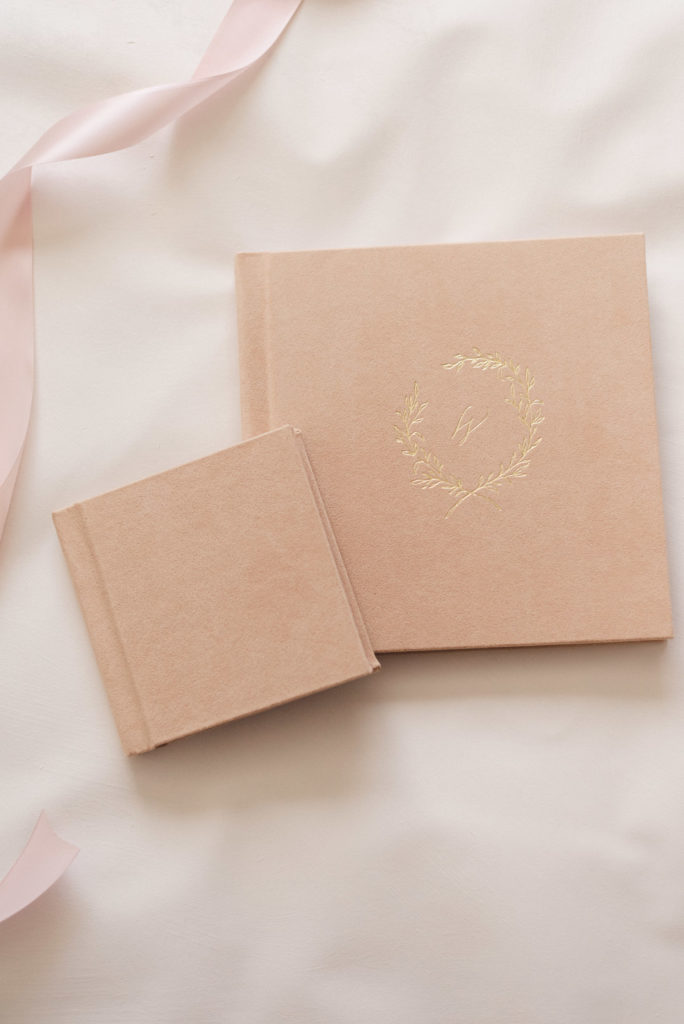 Heirloom album and a duplicate mini album made of blush vegan suede and gold debossing containing phoenix newborn baby photography.
