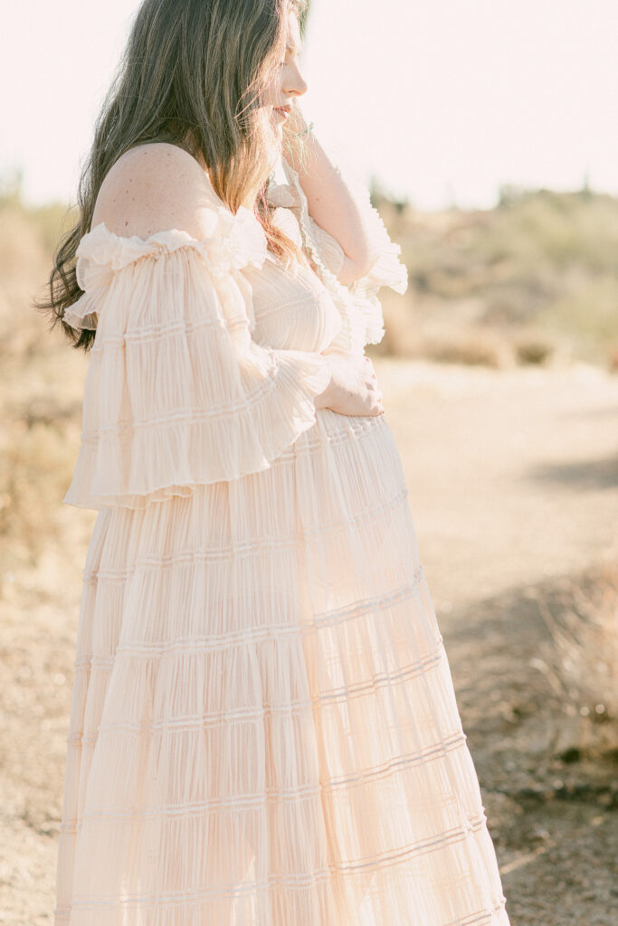 Scottsdale desert maternity photo of mom in blush pink chiffon dress. One hand is on baby bump and the other through her hair