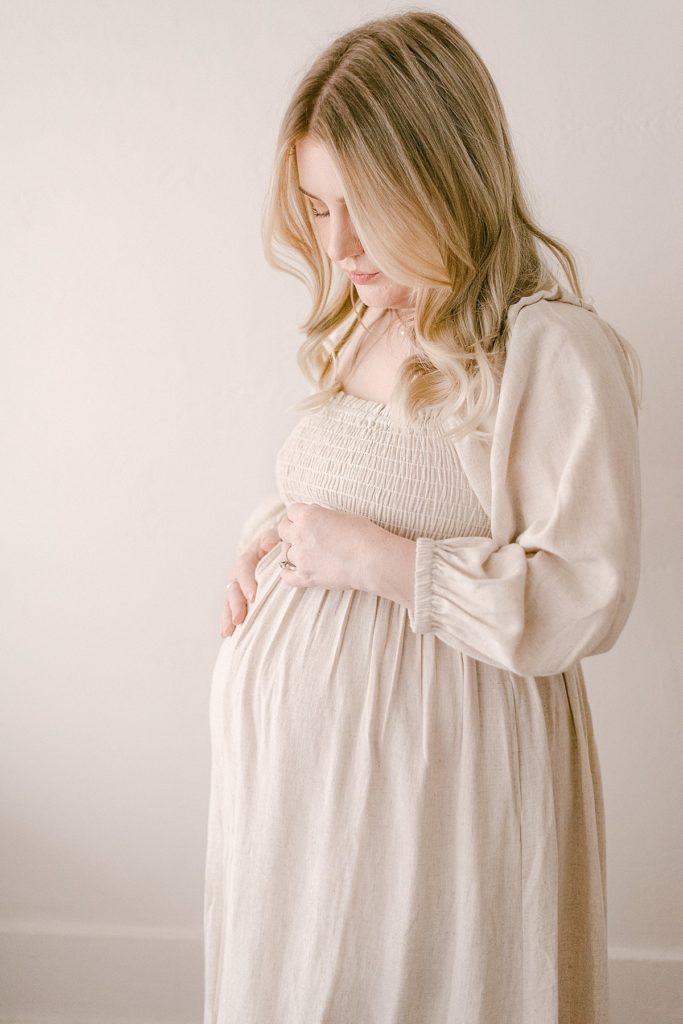mom in flowy dress holding baby bump for scottsdale photographer documenting an in-studio maternity sessiono