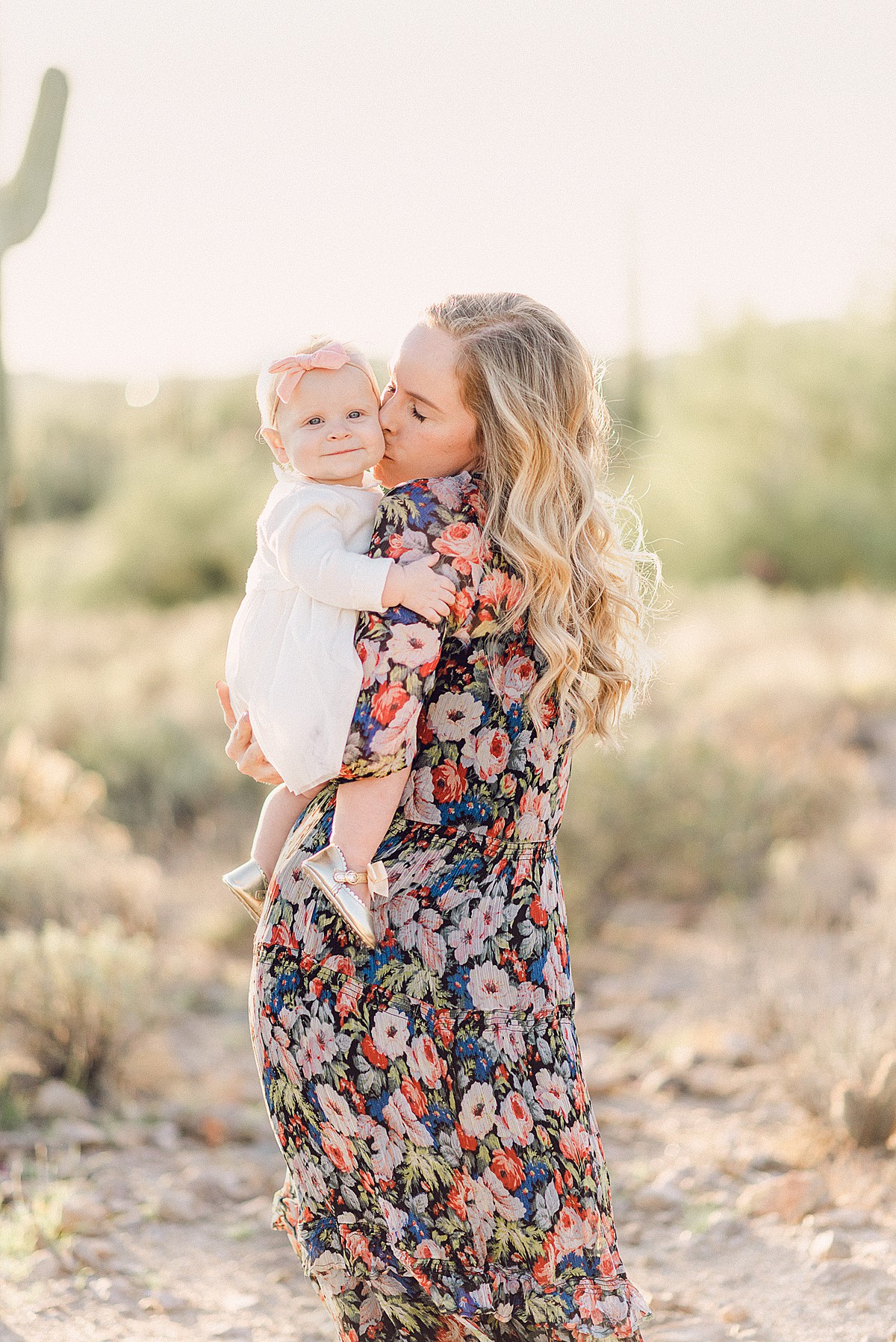 Mommy and me photoshoot in Phoenix desert with baby girl. Mom is wearing a floral patterned dress and 6 month baby girl in white dress.