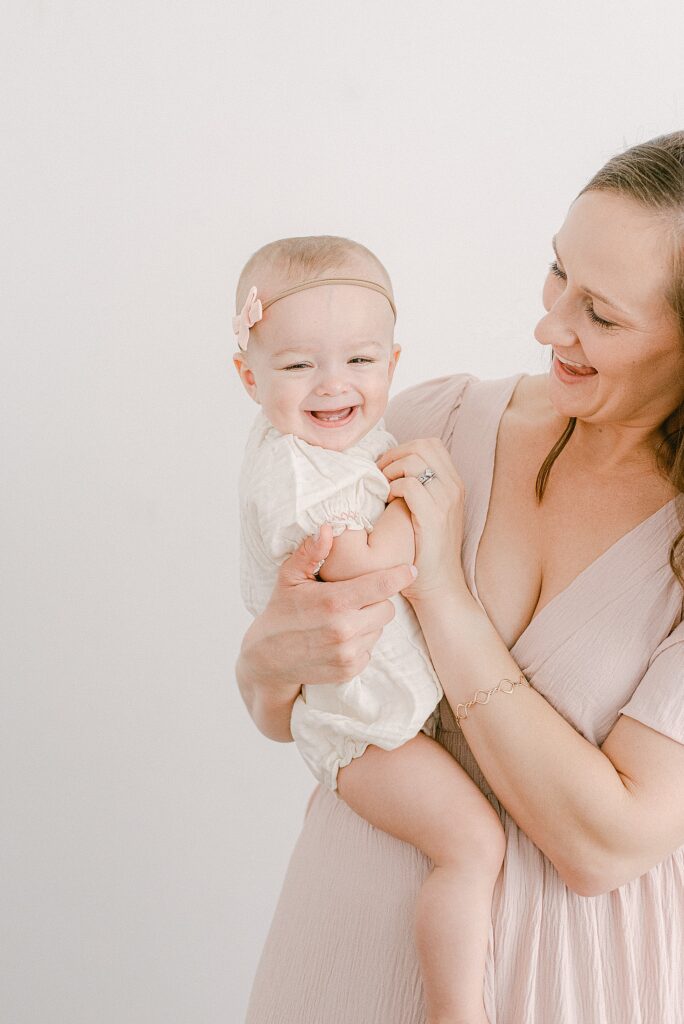 mom wearing pink blush dress holding one-year-old in white romper