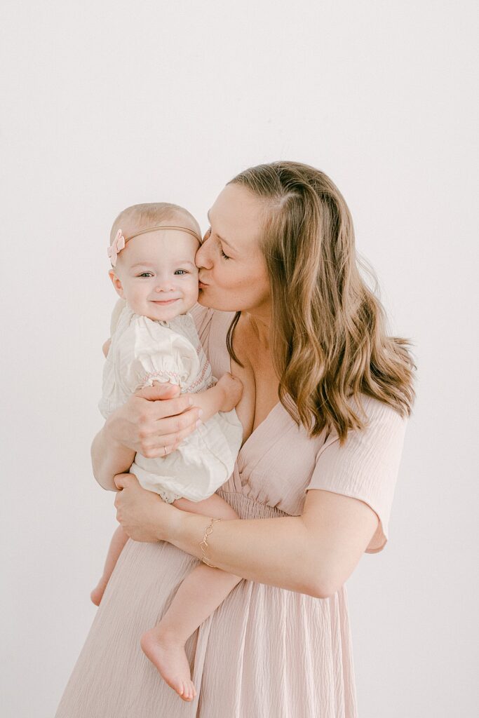 Mom kissing forehead of one-year old baby for cake smash photoshoot