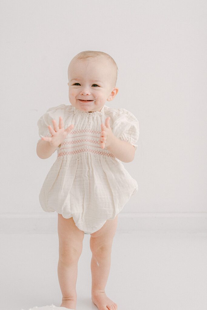 one-year-old baby standing and clapping in organic cotton white romper