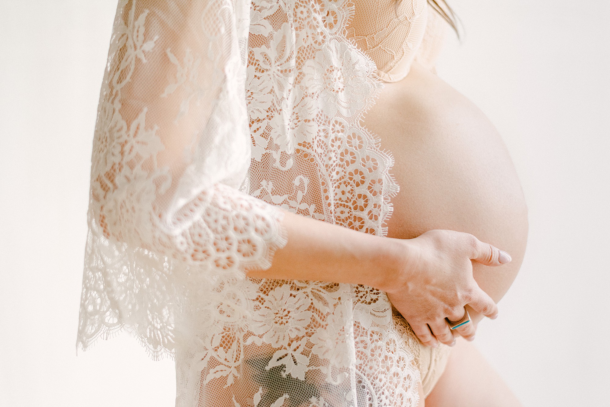 Closeup of baby bump with mom wearing white lace robe