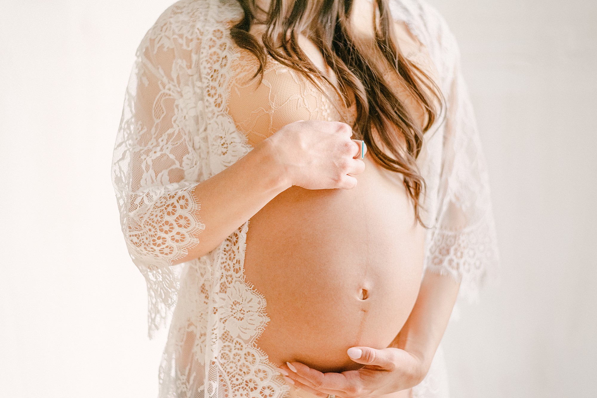 Closeup of baby bump in white lace robe with moms hands on top and bottom of baby bump