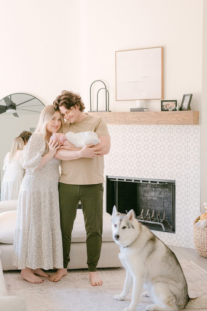 New parents holding baby in living room for Scottsdale lifestyle newborn photography session. Their siberian husky is standing at their feet.