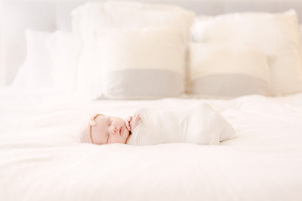 Scottsdale Lifestyle newborn photography session with baby wrapped in white swaddle on parents bed. 