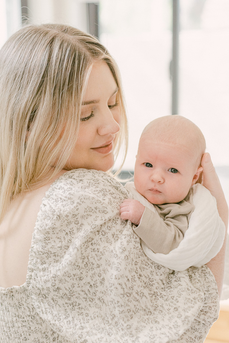 Newborn girl looking at camera over mom's shoulder. Mom is wearing flowy dress with floral pattern.