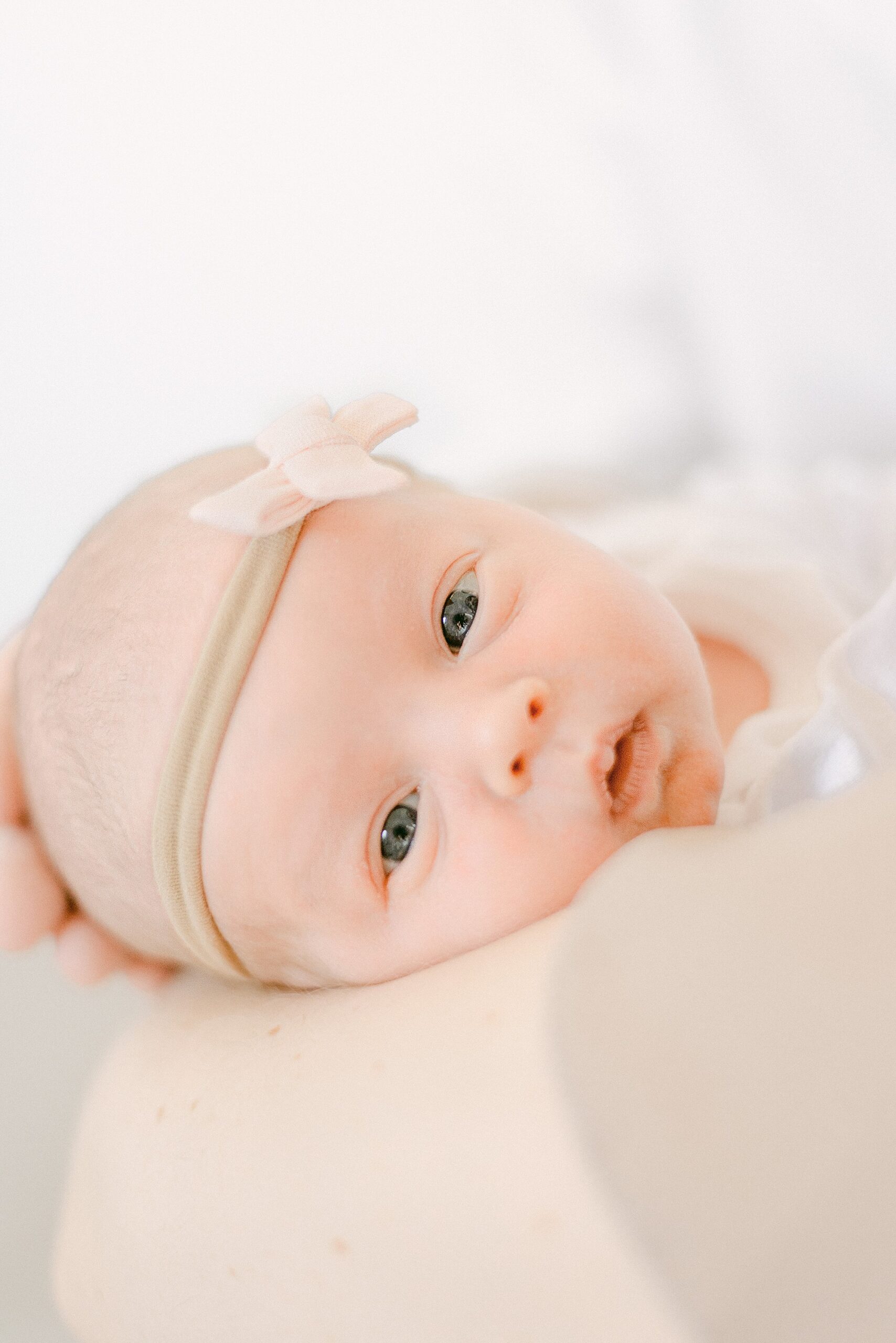 Newborn baby looking at camera while in mom's arms. She's wearing a pink bow headband
