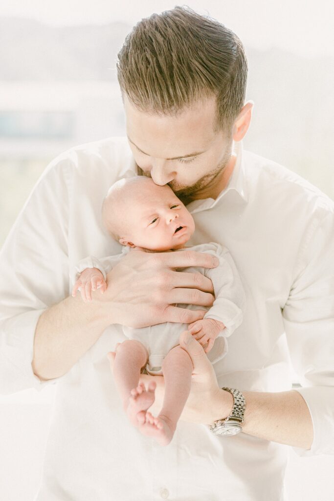 Dad holding newborn baby close to chest while kissing forehead