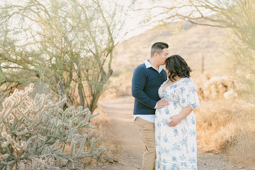 Dad kissing top of mom's head. Theyre standing between arch of desert bushes