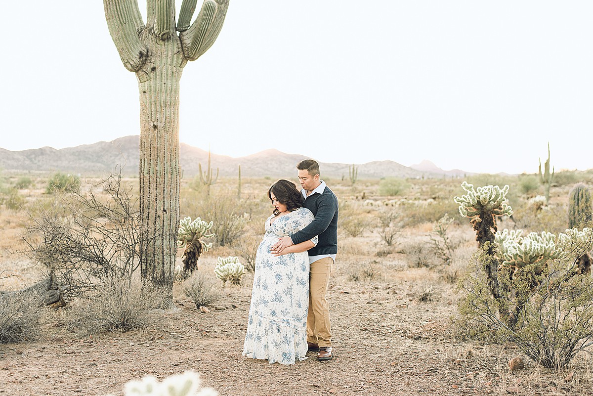 Fall maternity portraits in phoenix featuring a couple holding baby bump in desertscape during golden hour