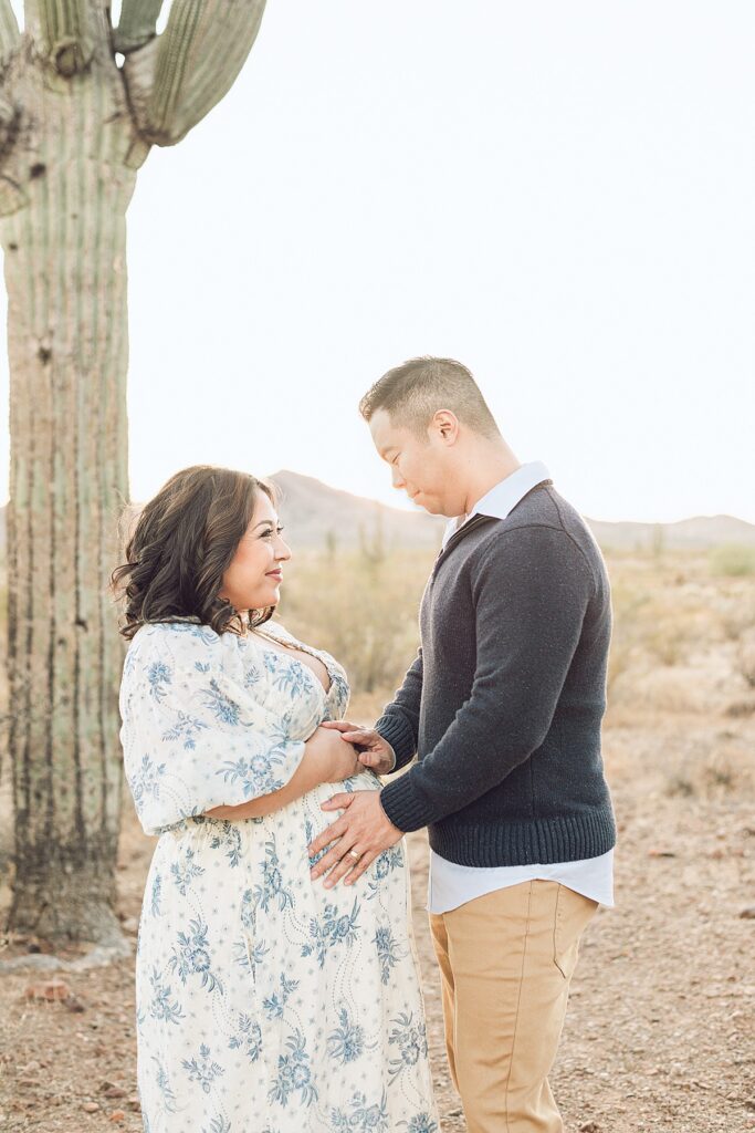 First time parents face to face while hands are on baby bump. Golden hour light is behind them.