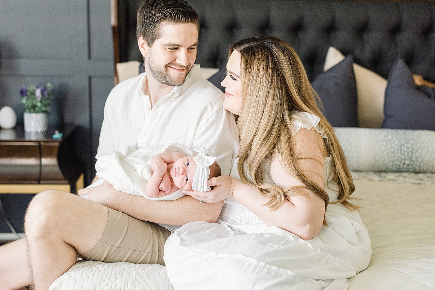 Chandler newborn photographer captures New parents holding newborn baby girl while smiling at each other on bed for lifestyle newborn session