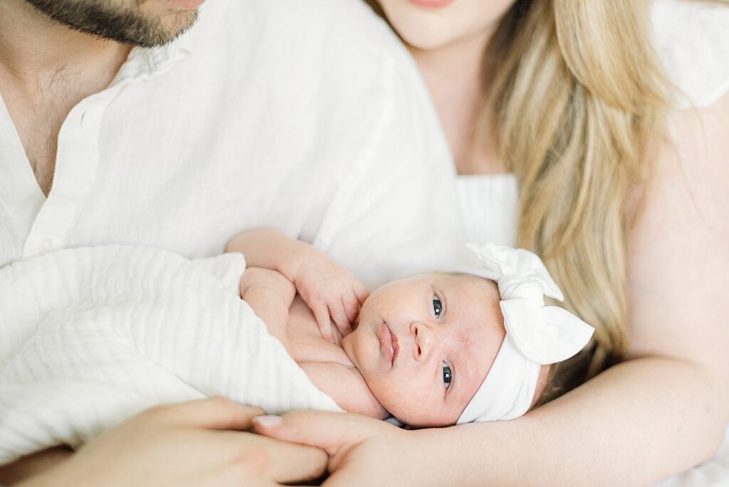 closeup of newborn baby looking at camera while parents are holding her.