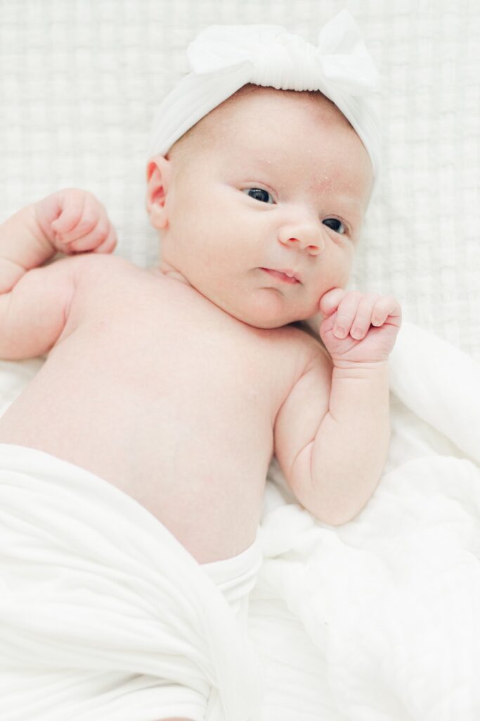 newborn baby girl is relaxed on white blanket while hands are curled near face