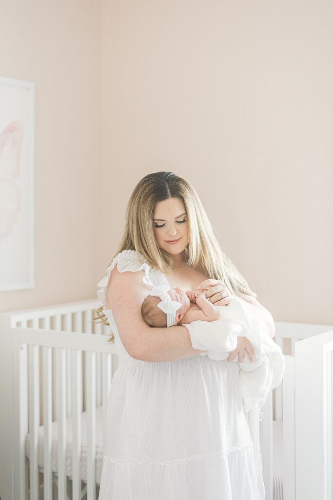 mom standing in pink nursery holding newborn baby