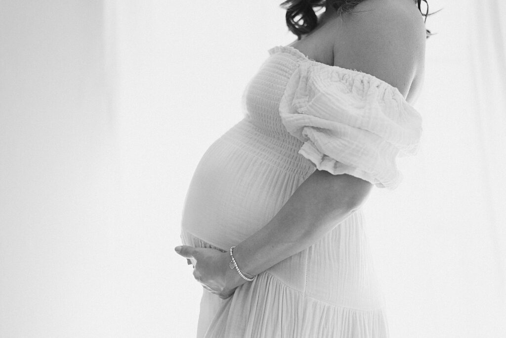 Queen Creek Photographer captures shoulder down view of baby bump. Mom's hand is cradling bump. 