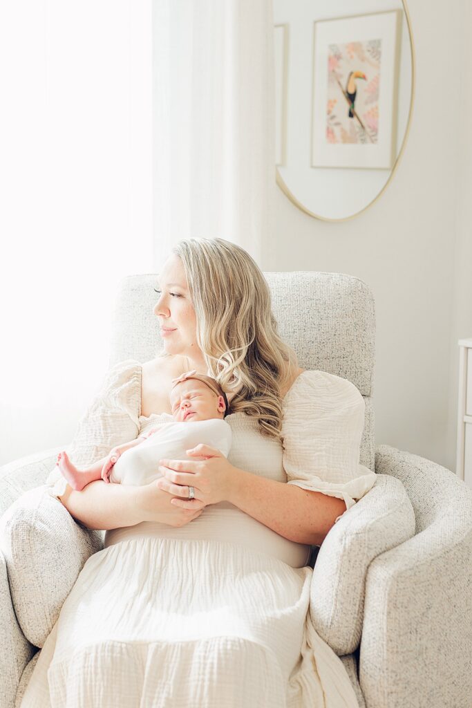 mom in nursery chair holding baby and gazing out window.