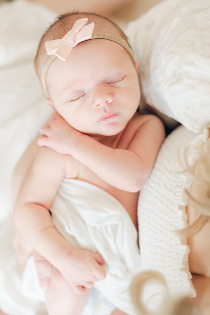 baby peacefully sleeping in mom's arms. baby's white swaddle is unraveling for lifestyle newborn photos