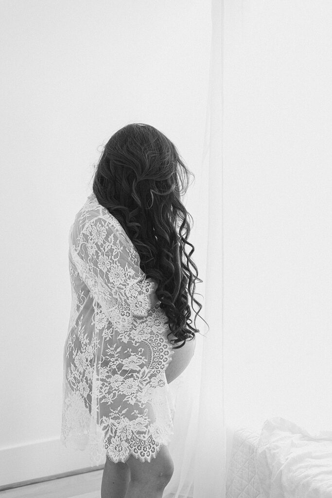 Expecting twin mom's baby bump pokes out of lace kimono robe with waist-length hair covering body