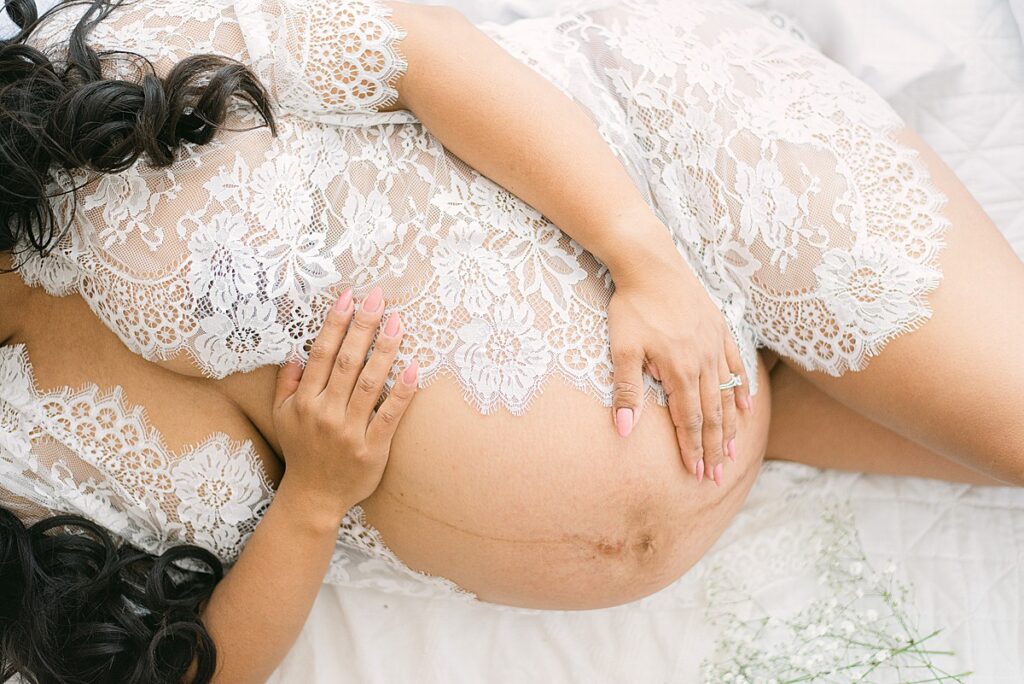 Expecting twin mom in lace robe while cradling hands around baby bump. 