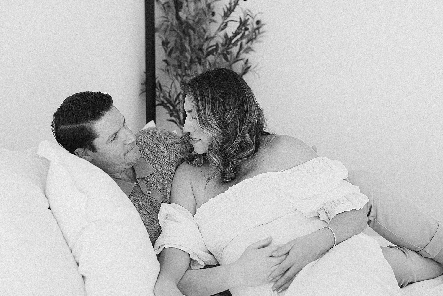 Expecting couple romantically embraced while on bed in Scottsdale studio for maternity photographs.