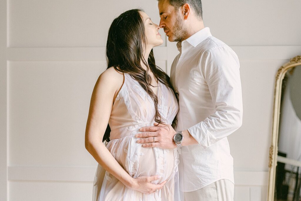 Couple nose-to-nose, each with a hand on mom's baby bump during maternity session before date night at the best Scottsdale Restaurants