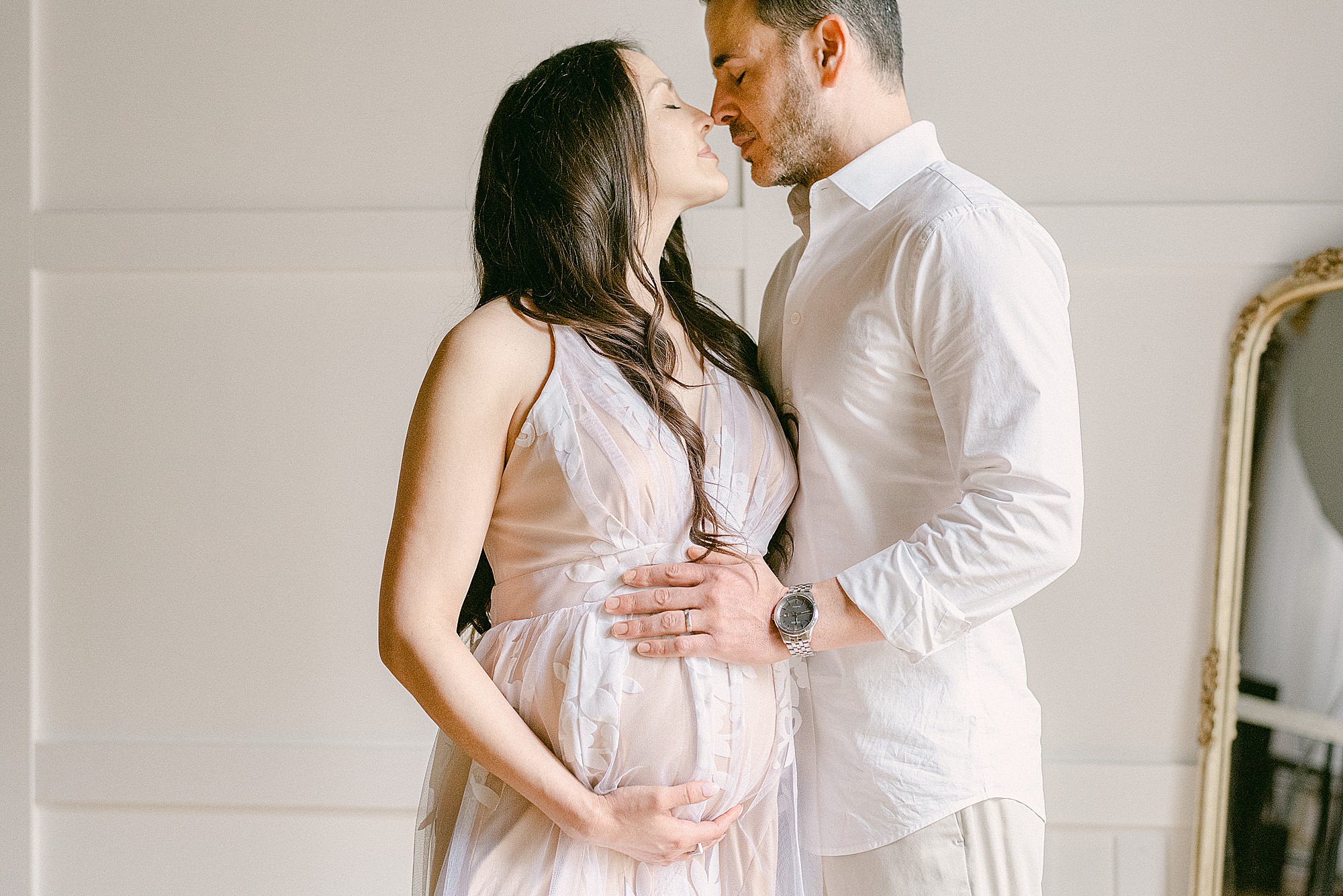 Couple nose-to-nose, each with a hand on mom's baby bump during maternity session before date night at the best Scottsdale Restaurants