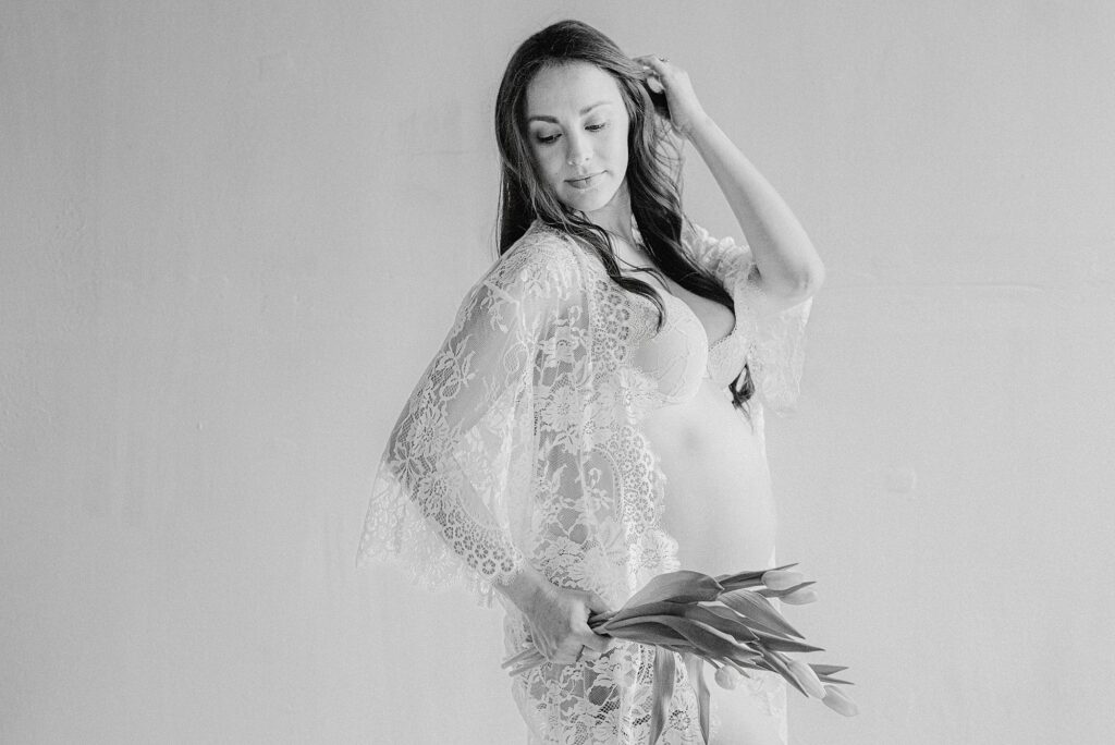 Pregnant boudoir photo of mom wearing lace kimono and holding tulips while running her hand through her hair. This is her maternity session before date night at the best Scottsdale Restaurants.