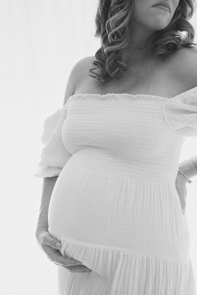 elegant view of baby bump with mom's hand under. her curls and lips are in frame