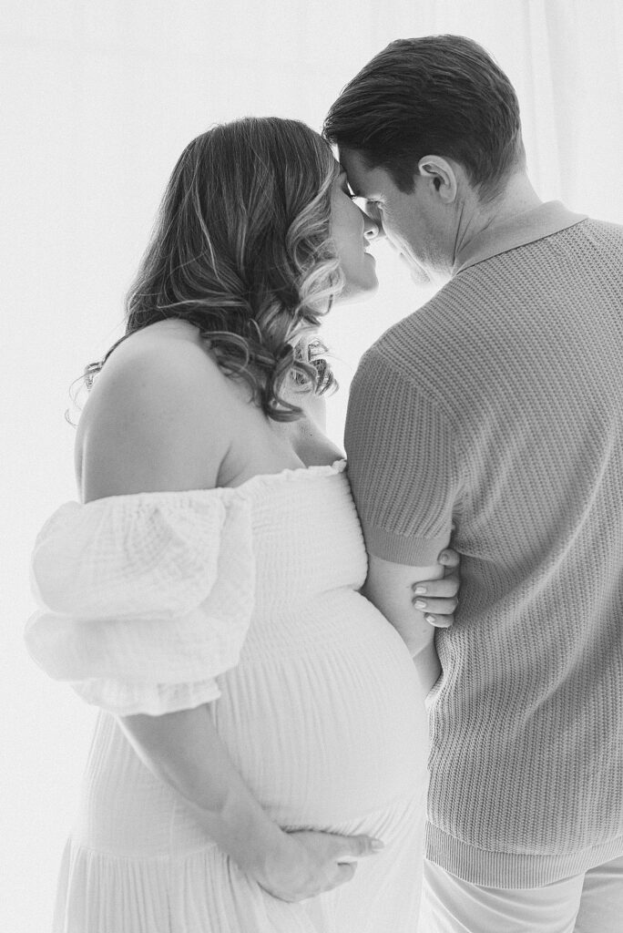 couple embraced and whispering from opposite directions. mom's hand is on baby bump in front.
